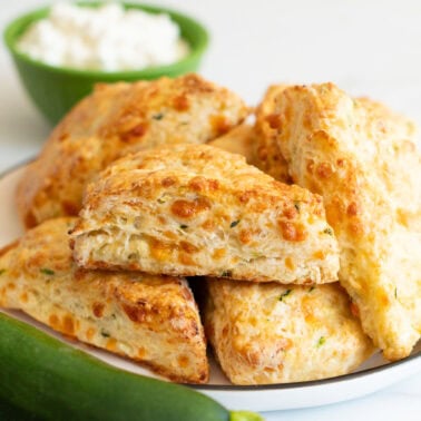Zucchini cheddar cottage cheese scones on a plate. A bowl with cottage cheese and zucchini on a counter.
