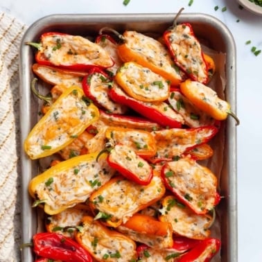 Baked and stuffed with cream cheese mini sweet peppers on a baking tray.