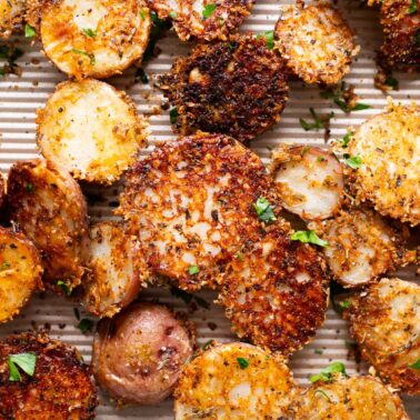 Crispy Parmesan potatoes garnished with parsley on a baking sheet.