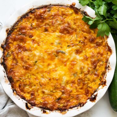 Crustless zucchini pie with parsley, zucchini and linen napkin on a counter.