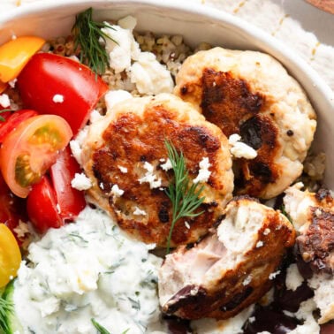 Greek turkey burgers served in a bowl with quinoa, vegetables and tzatziki.
