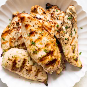 Grilled chicken breasts garnished with parsley and served on a plate.