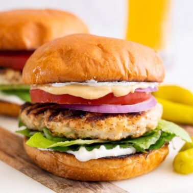 Grilled chicken burgers served on a marble platter with beer in the background.