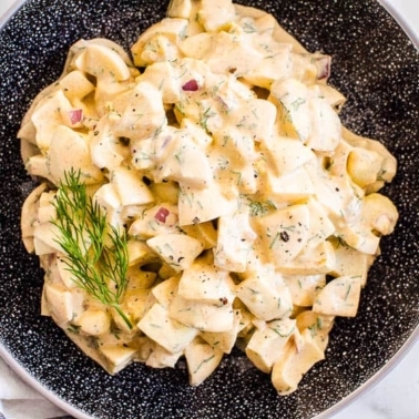 Healthy egg salad garnished with dill in black bowl.