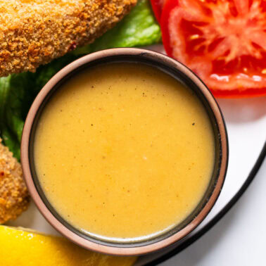Healthy honey mustard dressing in a bowl. Veggies and chicken strips on a plate.