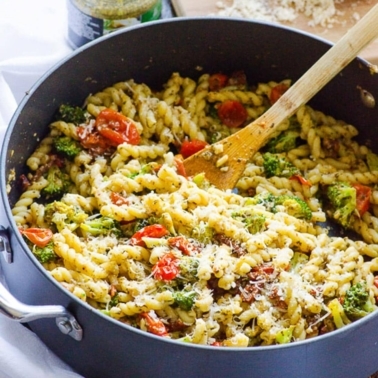 Healthy pasta recipe with tomatoes, broccoli and cheese in a skillet with a spoon.