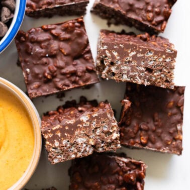 Cut up homemade crunch bars on a counter. Peanut butter and chocolate chips in bowls.