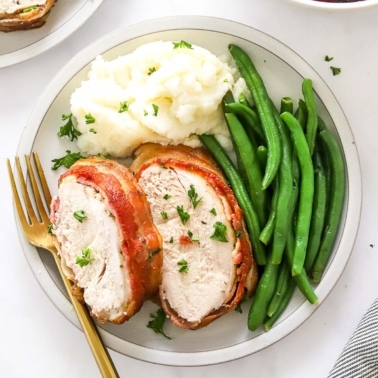 A plate with sliced turkey breast, mashed potatoes and green beans. Cranberry sauce in a bowl.