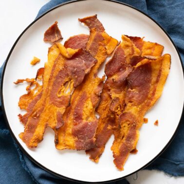 Baked bacon on white plate on top of blue linen.