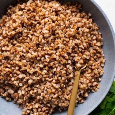 Cooked buckwheat groats served in a bowl with a spoon.