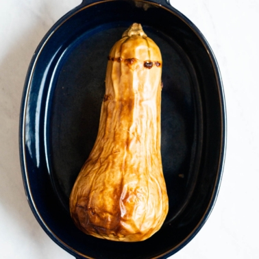 Roasted whole butternut squash in blue baking dish.