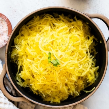 Black bowl with spaghetti squash noodles garnished with pepper and basil. Salt, pepper and towel nearby.