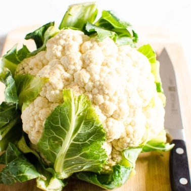 A head of cauliflower on cutting board with knife.