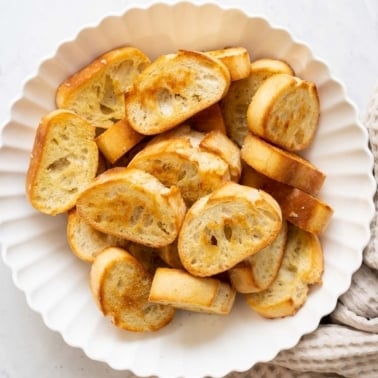 Homemade crostini in white bowl and towel nearby.
