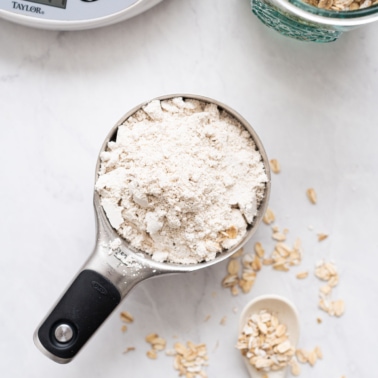 Oat flour in a measuring cup. Oats and scale nearby.