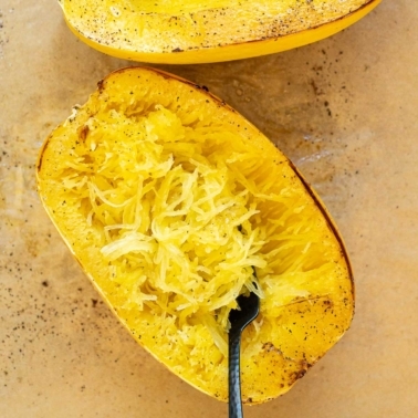 Spaghetti squash noodles fluffed up with a fork inside shell on a baking tray.