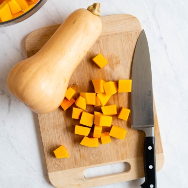 Cubed butternut squash on a cutting board with a knife and whole squash.