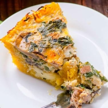 A slice of spaghetti squash quiche with a fork on white plate.