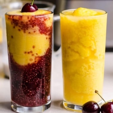 Two glasses with kombucha smoothie topped with cherry and cherries on a counter.
