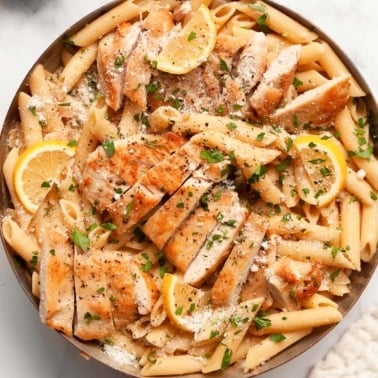 Lemon chicken pasta garnished with Parmesan cheese and parsley in a skillet.