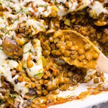 Lentil casserole with melted cheese on top and wooden spoon in baking dish.