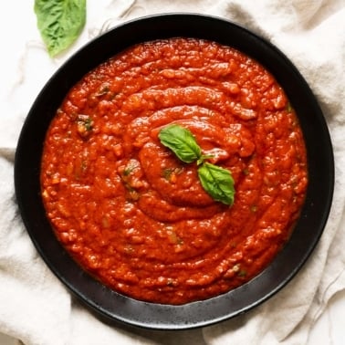 Marinara sauce in black bowl garnished with fresh basil leaves.