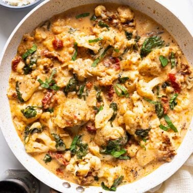 Marry me cauliflower in sun dried tomato sauce garnished with basil in a skillet.