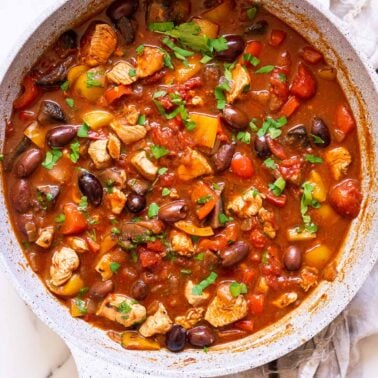 Mediterranean chicken skillet with peppers and olives in tomato sauce garnished with parsley.