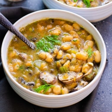 Bean mushroom soup with dill served in a bowl with a spoon.