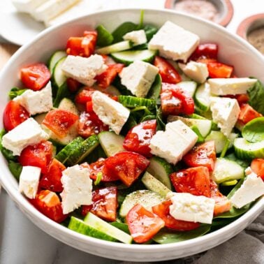 Spinach salad with cucumbers, tomatoes and feta cheese in a bowl.