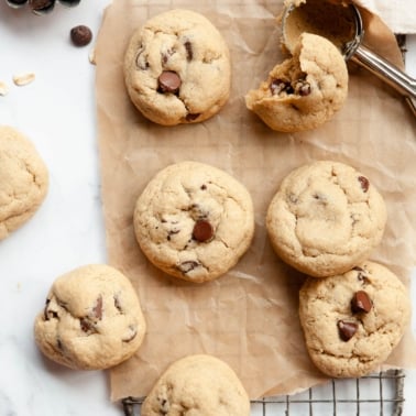 Oat flour chocolate chip cookies on a cooling rack. Cookie scoop and chocolate chips nearby.