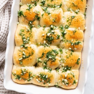 Pampushky with garlic dill oil on top in a baking dish.