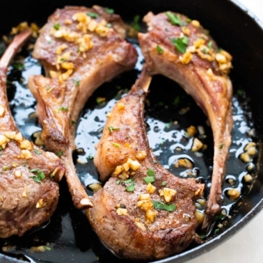 Four pan fried lamb chops with garlic butter and parsley in cast iron skillet.