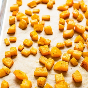 Roasted butternut squash cubes on parchment lined baking sheet.
