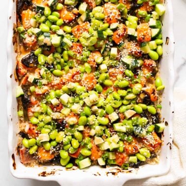 Salmon sushi bake with edamame beans, cucumber, green onion and sesame seeds in a baking dish.