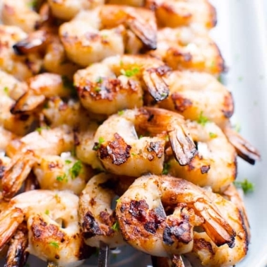 Grilled shrimp skewers garnished with parsley on a platter.