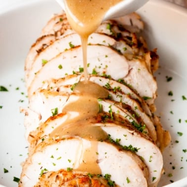 Pouring gravy on top of sliced slow cooker turkey breast.