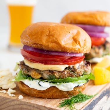 Spinach feta turkey burgers served on a wooden board with beer in a glass in a background.
