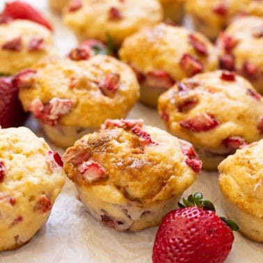 Strawberry muffins on parchment paper with fresh strawberries around them.
