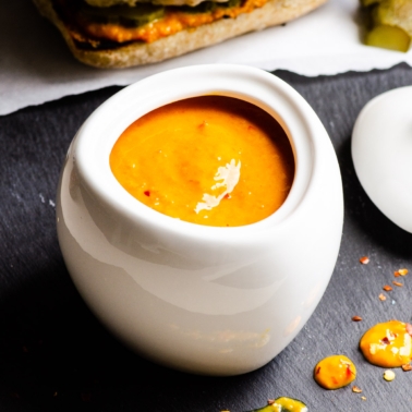Sweet and spicy mustard in white jar. Burger and pickle on a side.
