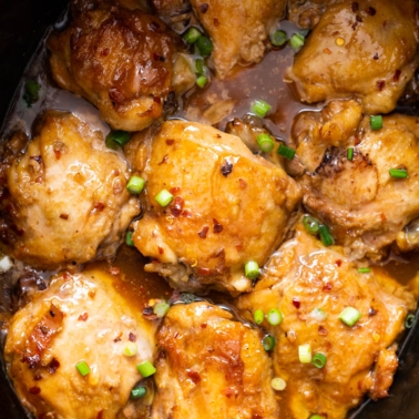 Thai chicken thighs in crock pot garnished with green onions.