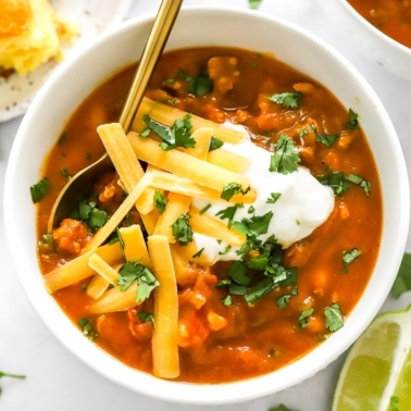 White bean pumpkin turkey chili garnished with cheddar cheese and cilantro in white bowl.