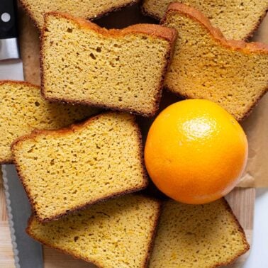Slices of whole orange blender cake on a cutting board with whole orange and knife next to it.
