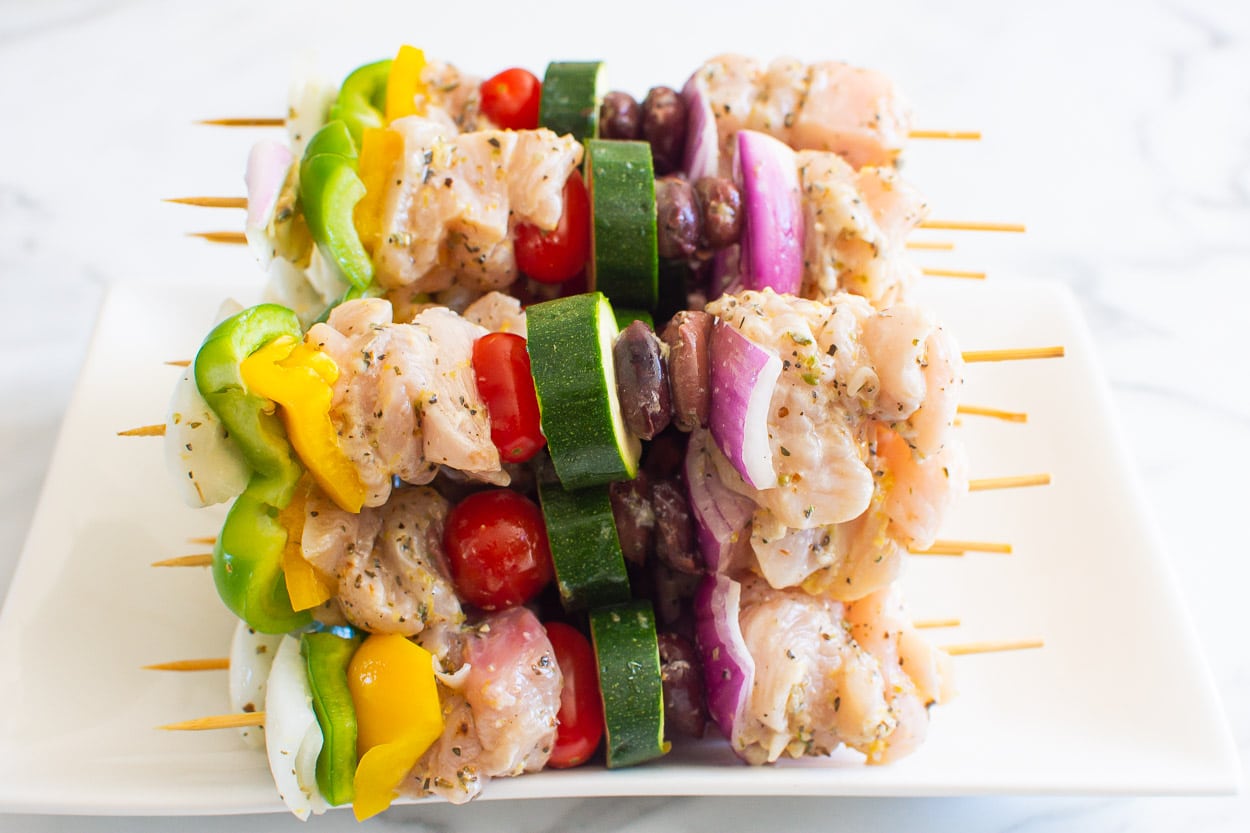 Raw chicken kabobs on platter.