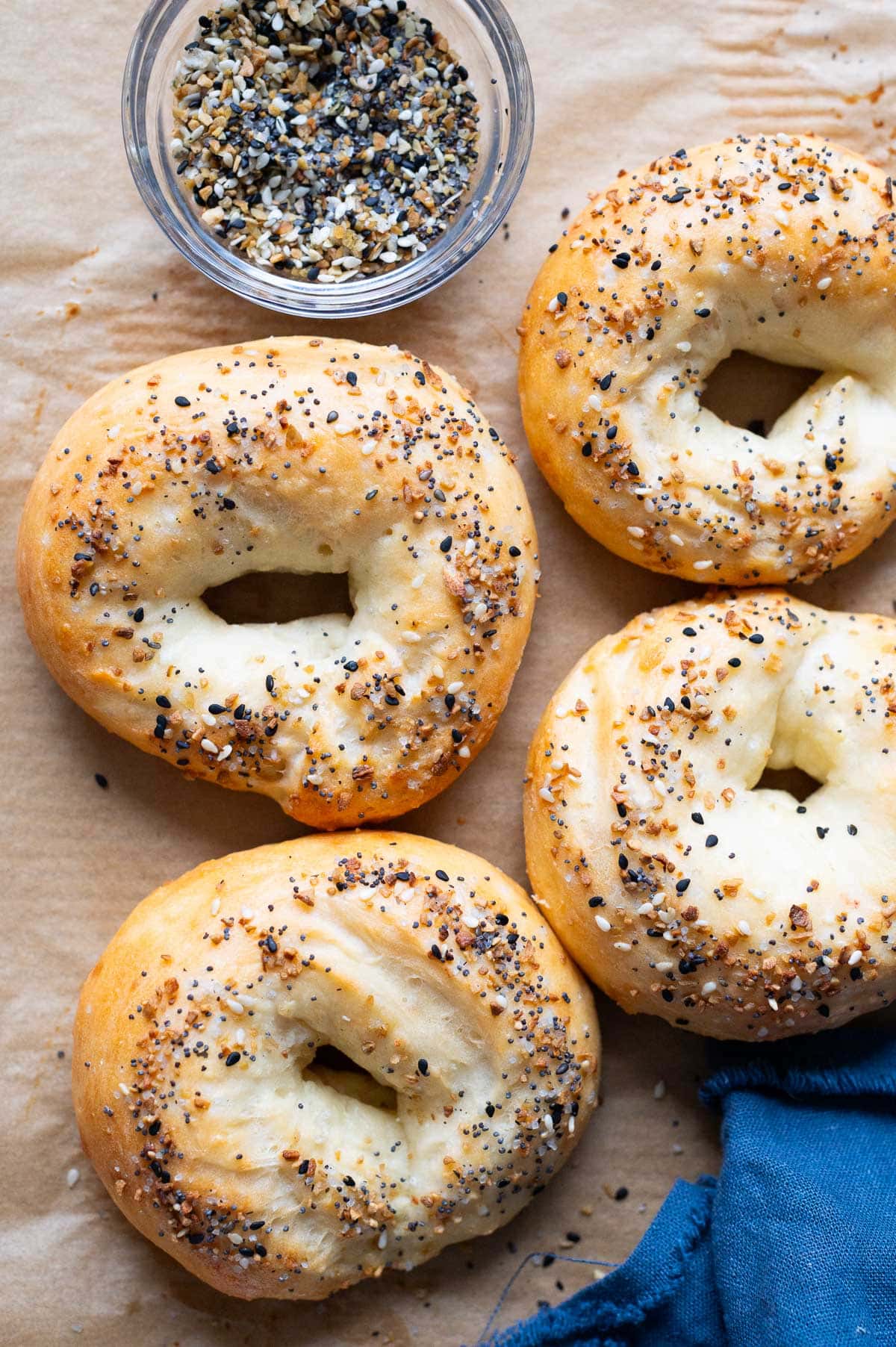 4 Greek yogurt Bagels on a baking sheet. A bowl with everything bagel seasoning and blue napkin.