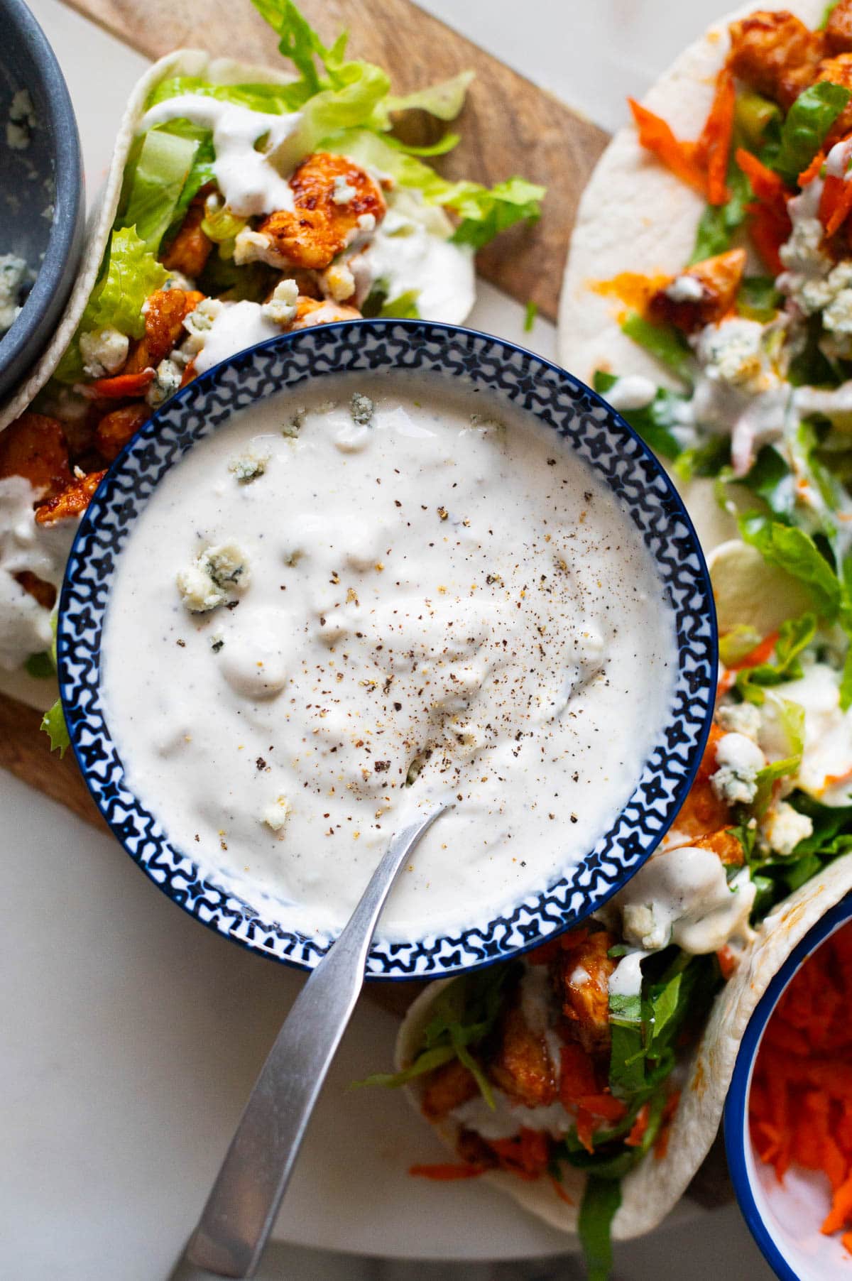 Greek yogurt blue cheese dressing in a bowl with a spoon. Buffalo chicken tacos on a serving platter.