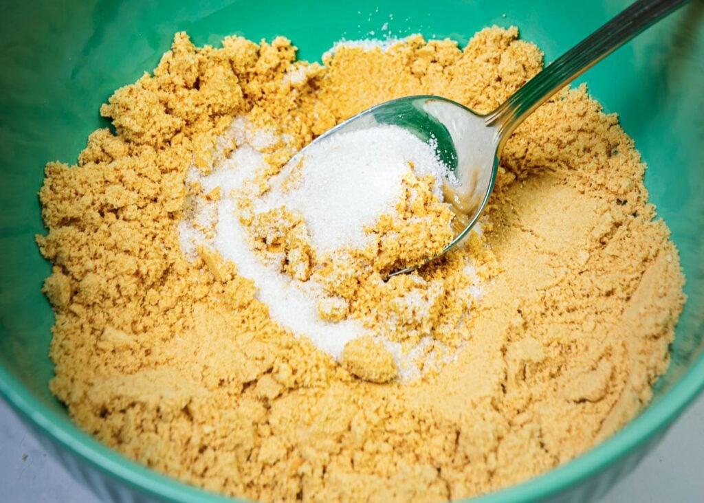 Graham cracker crumbs and sugar in green bowl.