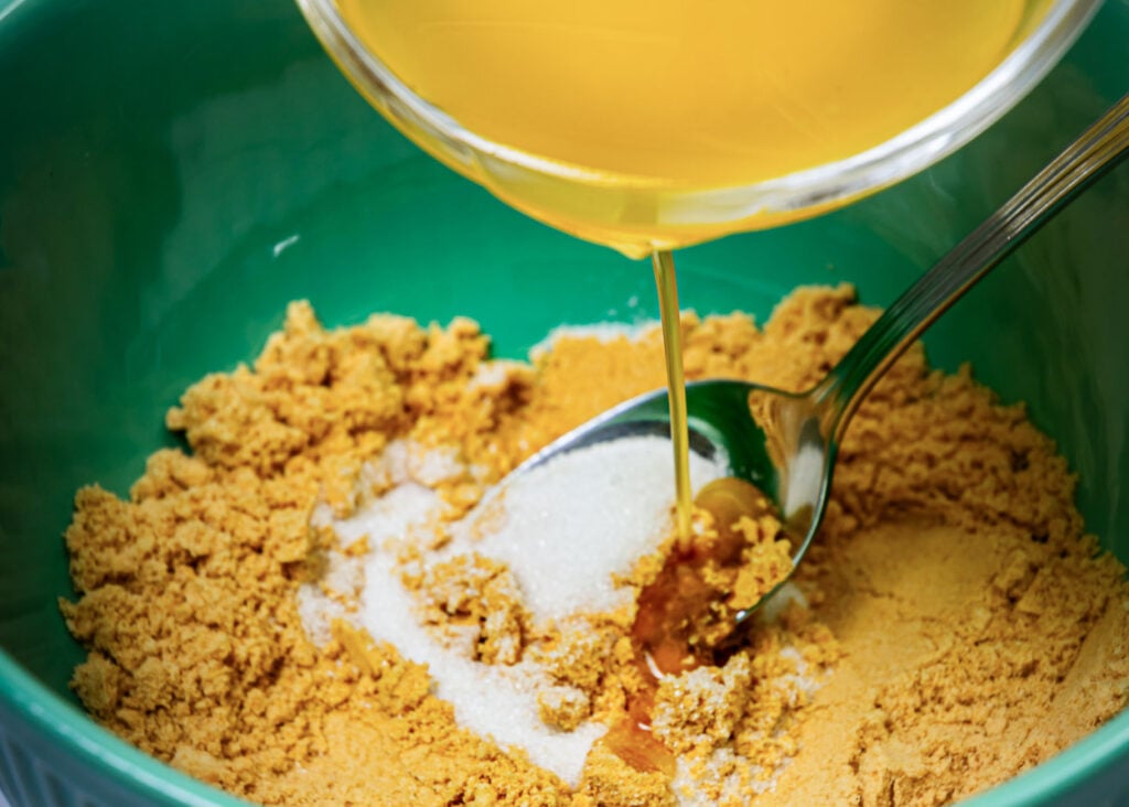 Melted butter being poured into bowl with graham cracker crumbs and sugar.