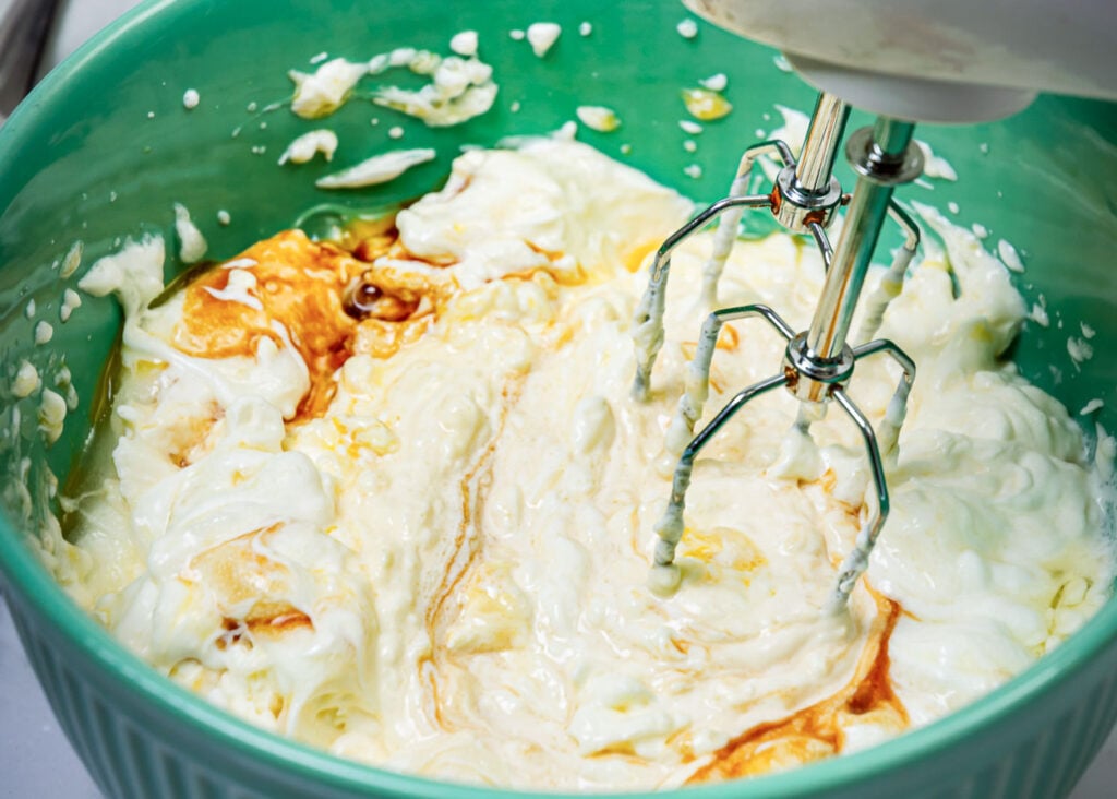 Using electric mixer to whip cream cheese, greek yogurt, eggs and vanilla in a bowl. 