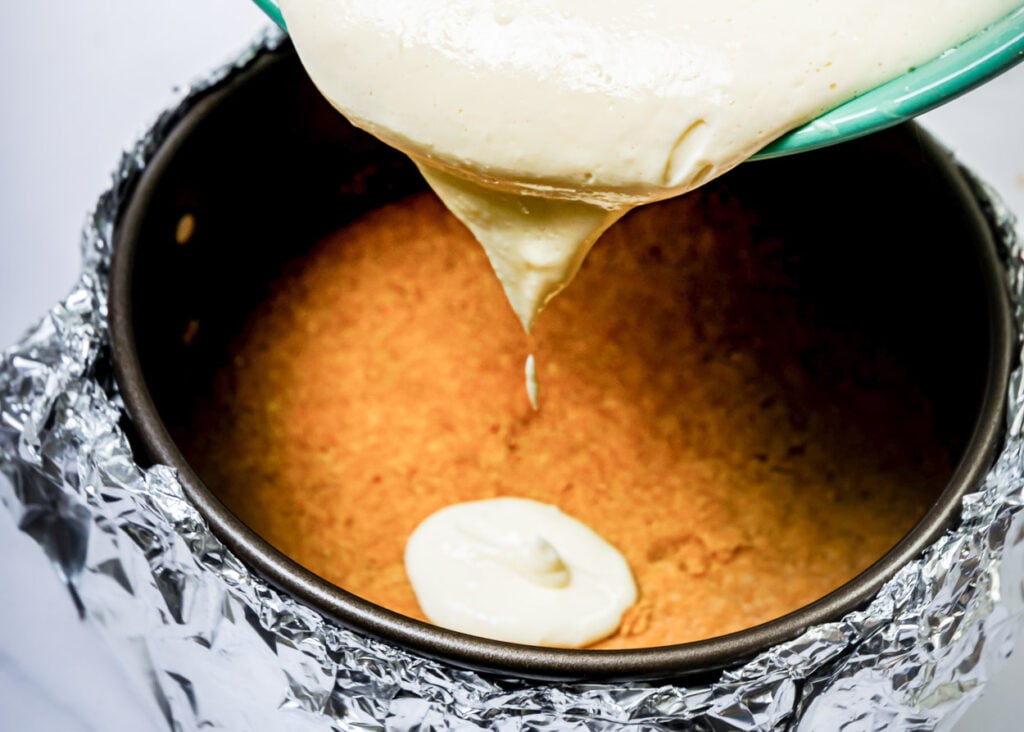 Pouring cheesecake mixture on top  of crust into springform pan.